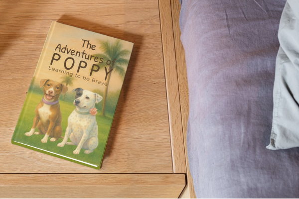 Book titled 'The Adventures of Poppy' on a wooden floor with a person's leg in the background.
