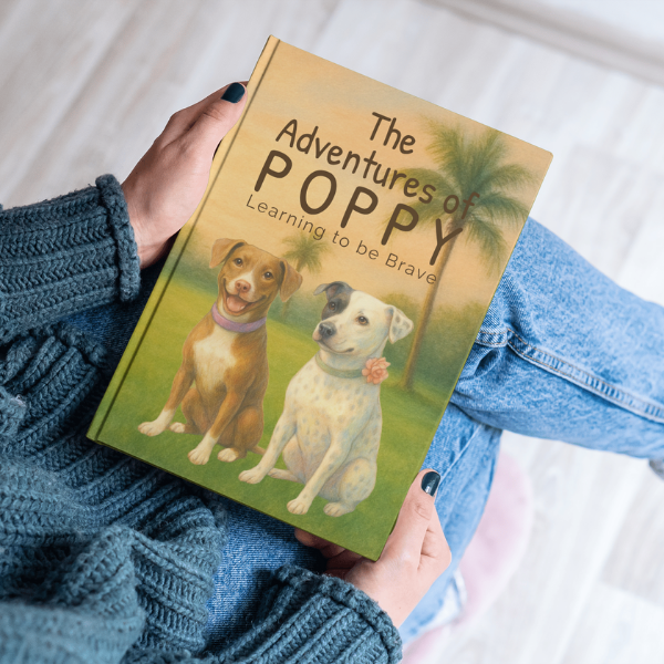 Book titled 'The Adventures of Poppy: Learning to be Brave' held by a person wearing blue jeans and a blue sweater.